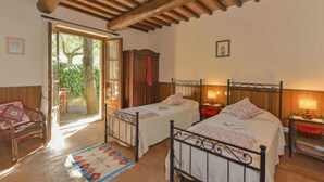 Een kamer met twee bedden, houten balkenplafond, een groot raam en uitzicht op groen.