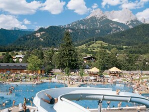Ein Schwimmbeckenbereich mit mehreren Pools, umgeben von Gebäuden und einer Bergkulisse.