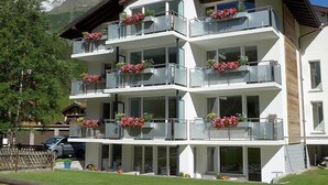 Ein mehrgeschossiges Hotel mit Balkonen, die mit Blumen geschmückt sind, vor einer Bergkulisse.