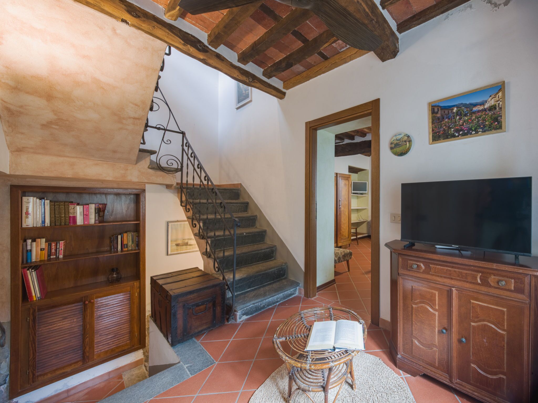 Ein gemütliches Wohnzimmer mit einer Treppe, Holzregalen, einem Korbstuhl, einem Fernseher und einem Gemälde an der Wand.