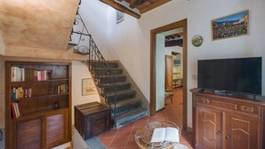 A cozy living room with a staircase, wooden bookshelves, a wicker chair, a television, and a painting on the wall. - Casa di Nena by Interhome (Camaiore)