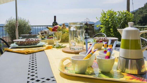 A table set outdoors with a view of the sea, a white umbrella, and various dining items. - Casa di Nena by Interhome (Camaiore)