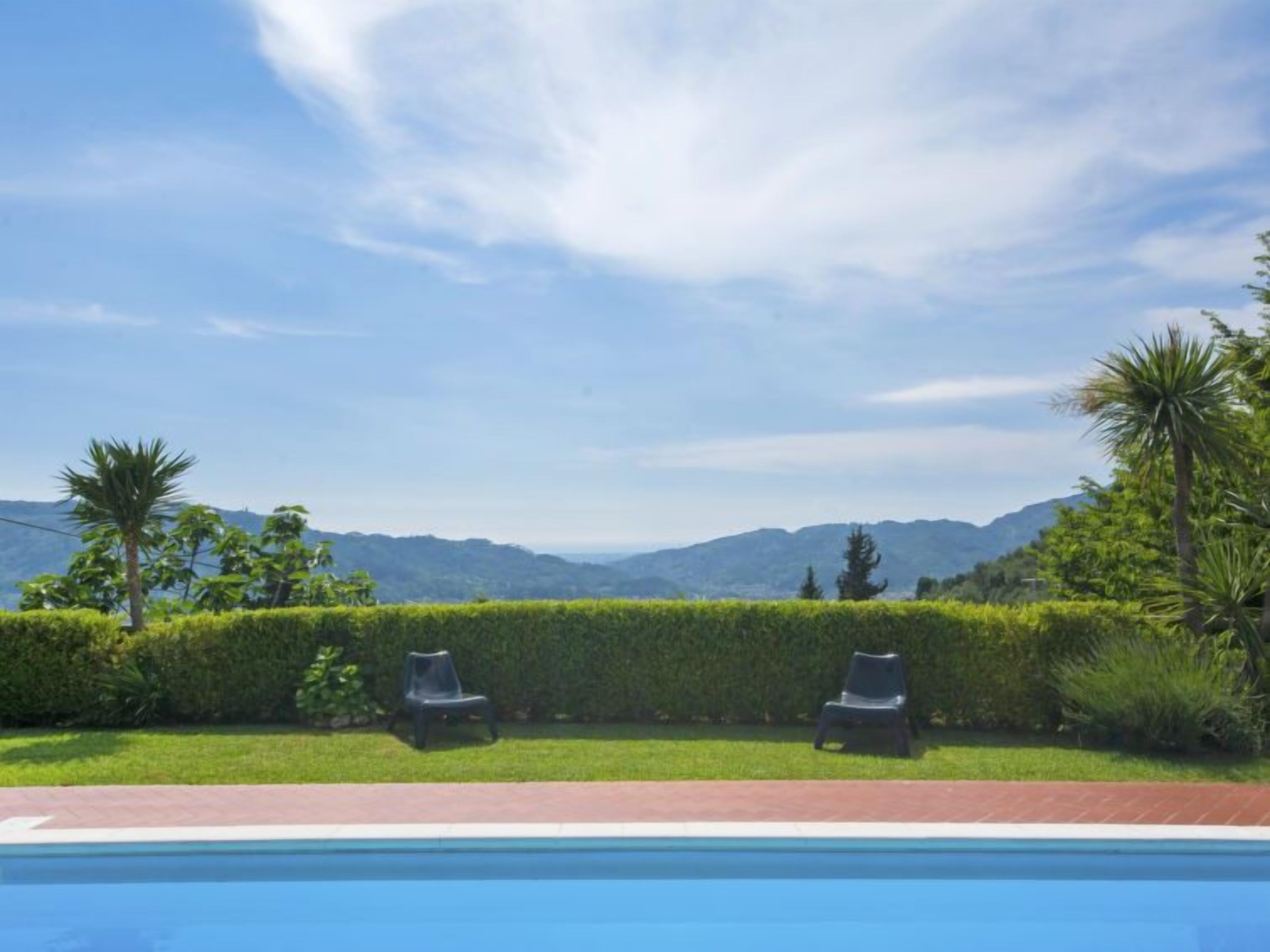 Una piscina con due lettini e un siepe in primo piano, con un paesaggio montuoso sullo sfondo.