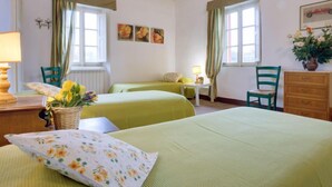 A room with two beds, a wooden ceiling, a window with curtains, a chair, a table, and a vase with flowers. - San Bernardino by Interhome (Barga)