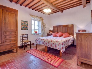 Ein Schlafzimmer mit einem hölzernen Bett, einem Nachttisch, einem Stuhl, einem Kleiderschrank und einem Fenster mit Vorhängen.