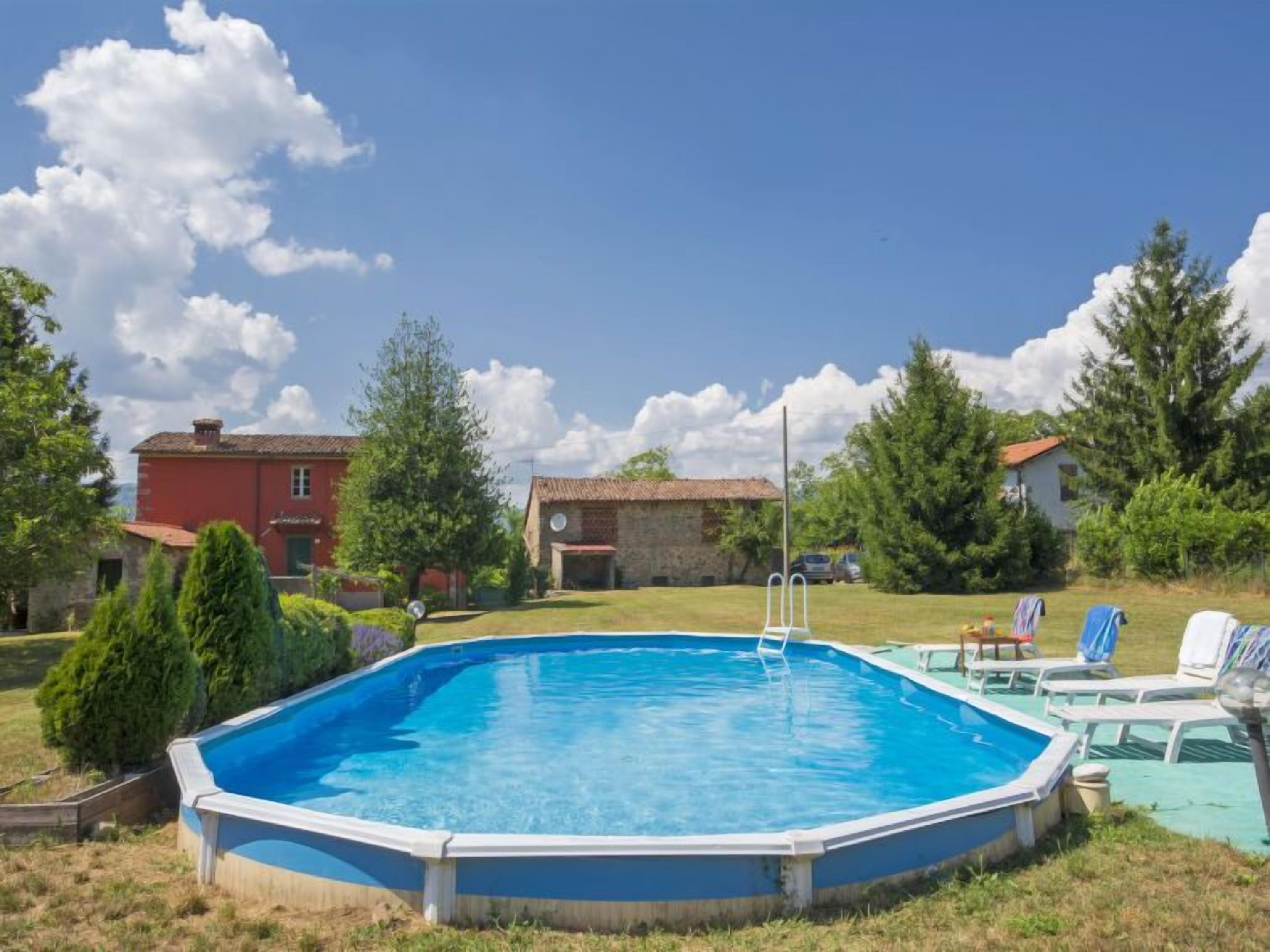 Une piscine extérieure avec un escalier, entourée de pelouse et d’arbres, avec des maisons en arrière-plan.