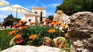 A building with a flat roof and a white facade, surrounded by greenery and orange flowers. - Tenuta Nucci by Interhome (Gallipoli)