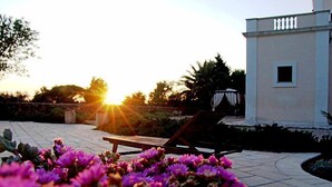 A patio with a sunlit view, a lounge chair, and a building with a small window. - Tenuta Nucci by Interhome (Gallipoli)