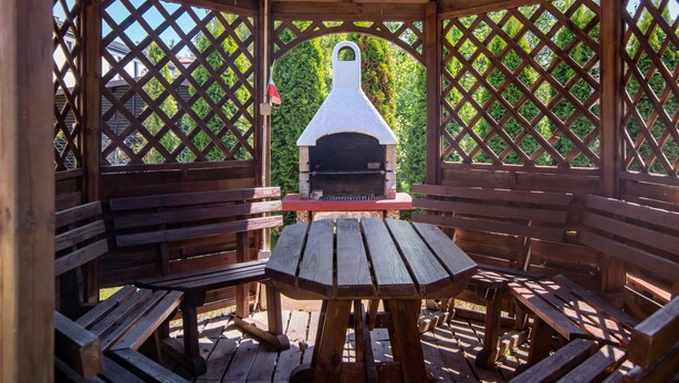 A wooden gazebo with a central grill table and benches, surrounded by a lattice fence. - Mały dworek by Interhome (Leba)