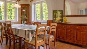 A dining area with a wooden table and chairs, large windows, and a painting on the wall. - Mały dworek by Interhome (Leba)