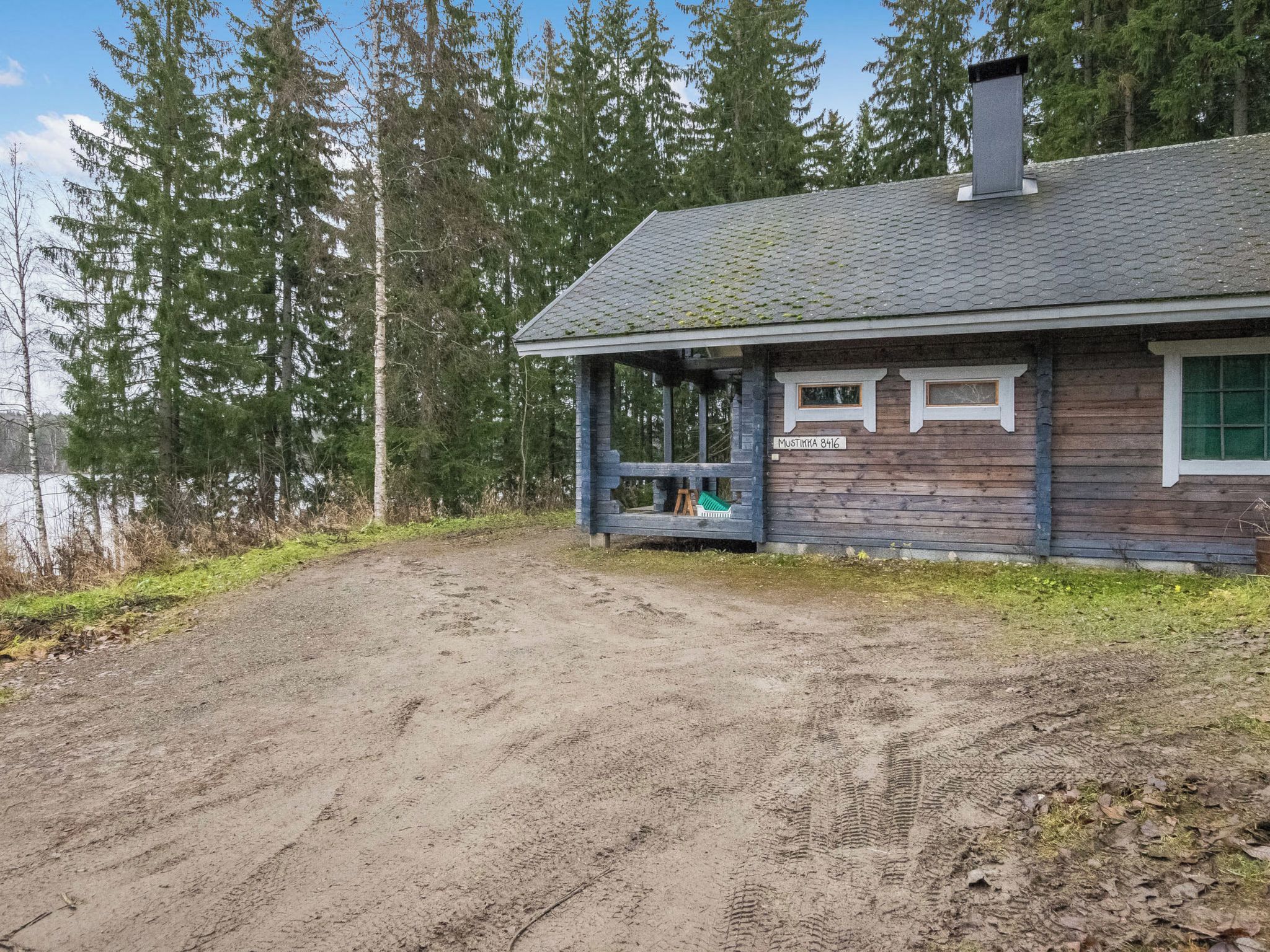 A rustic cabin with a wooden exterior, a porch, and a dirt driveway.