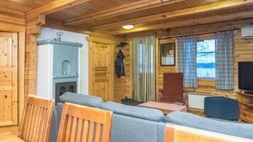 Interior acolhedor de uma cabana com sofá, paredes de madeira, lareira e televisão.