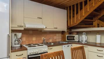 A kitchen with white cabinets, a stove, a sink, a microwave, and a wooden staircase.