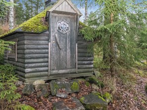 A rustic log cabin with a hexagonal door, surrounded by a forest.