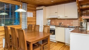 A wooden cabin interior with a dining table, chairs, a kitchen area including a stove, sink, and cabinets, and a window with curtains. - Mustikka by Interhome (Hämeenlinna)
