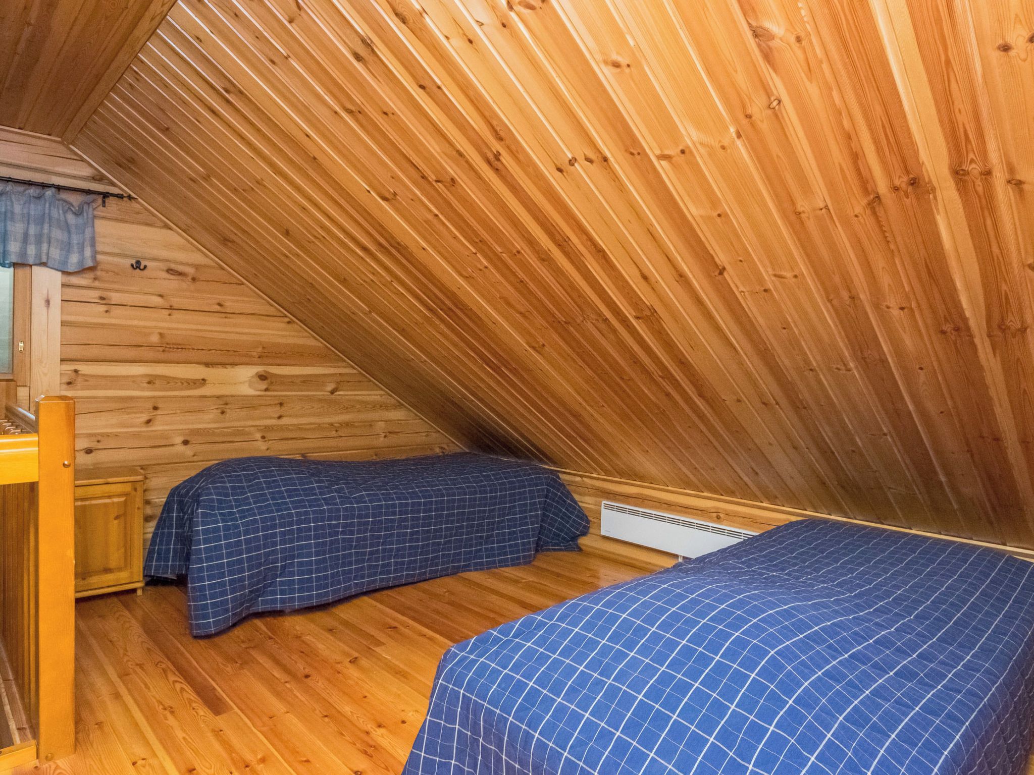Ein kleines Schlafzimmer im Dachgeschoss mit Holzbalken an der Decke, zwei Betten mit blauer Bettwäsche, einem hölzernen Schminktisch und einem Heizkörper.