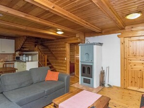 L’intérieur chaleureux d’un chalet avec un canapé, une cheminée, un coin cuisine et un escalier en bois.