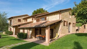 Une maison en pierre avec un patio, un petit jardin et une voiture garée devant.