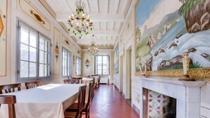 Ein langer Speisesaal mit hohen Decken, großen Fenstern und einem Landschaftsgemälde an der Wand.