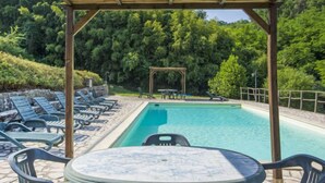 Ein Poolbereich mit Liegestühlen und einem Tisch, umgeben von einer Holzpergola und üppigem Grün.