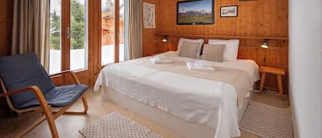 A wooden-paneled bedroom with a large bed, a chair, and a view of the outdoors.