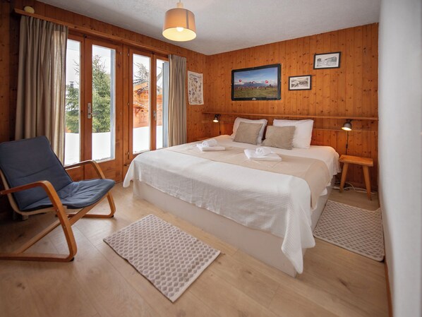 A wooden-paneled bedroom with a large bed, a chair, and a view of the outdoors.