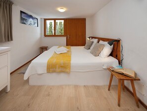 A bedroom with a bed, wooden headboard, a bedside table with a book, a window, and a painting on the wall.