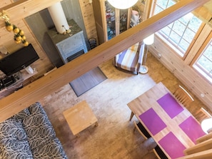 Een kamer met hoge plafonds en een houten vloer, een bed met een gestreept deken, een tafel met een paarse tafelkleed, en een televisie op een standaard.