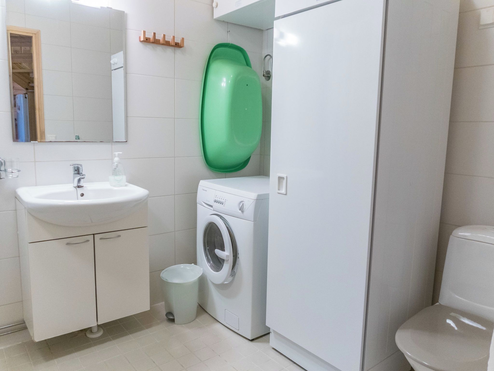 A bathroom with a sink, mirror, toilet, and a washing machine.