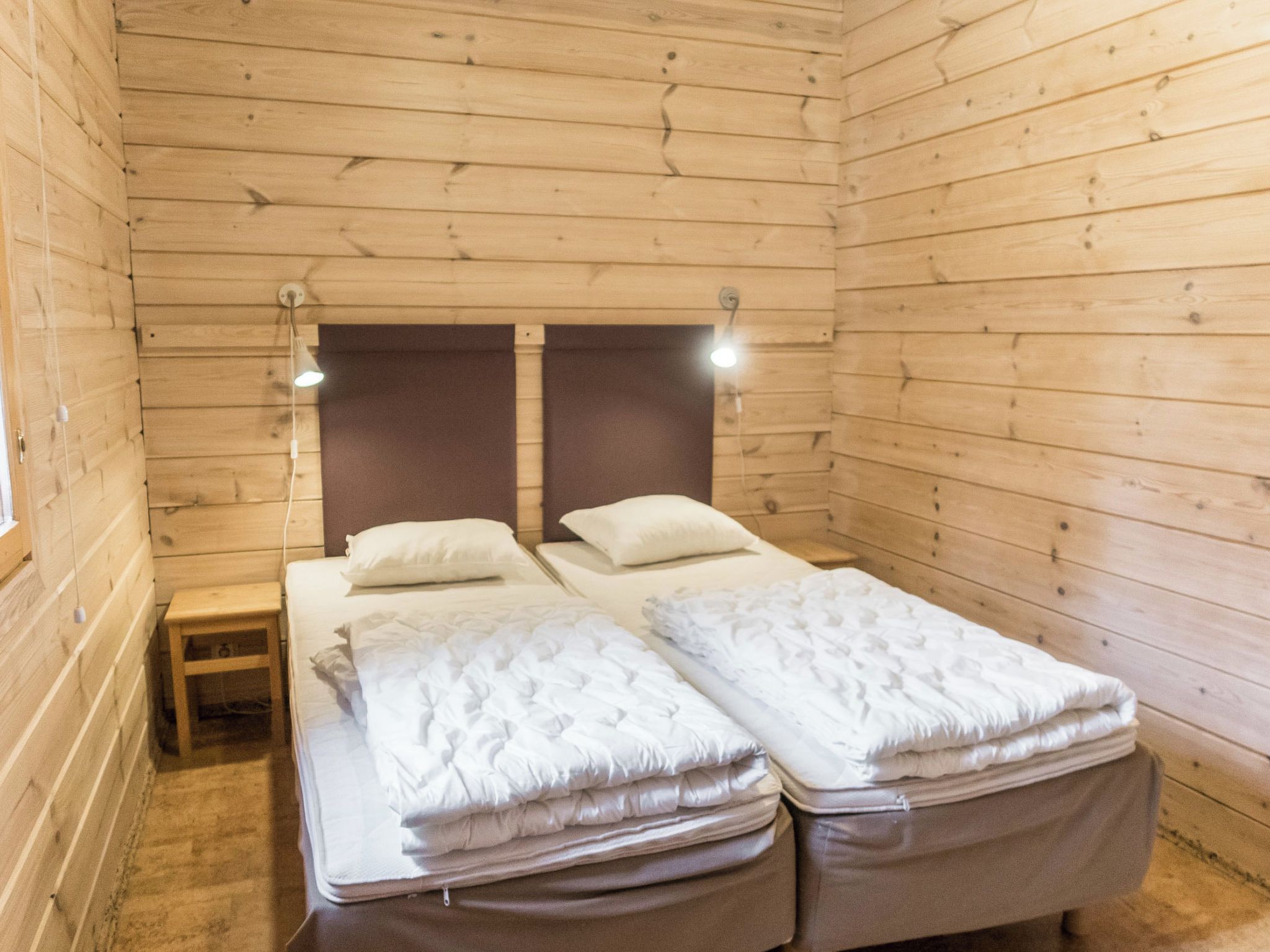 Una habitación de cabaña de madera con una cama, una mesita de noche y dos lámparas fijadas a la pared.