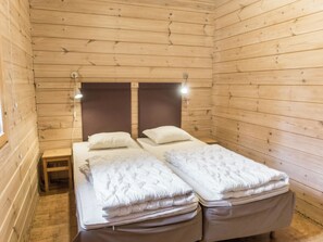 Una habitación de cabaña de madera con una cama, una mesita de noche y dos lámparas fijadas a la pared.