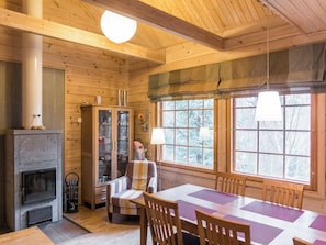 Un interior de cabaña acogedor con chimenea, paredes de madera, una mesa de comedor y ventanas amplias.