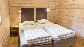 A wooden cabin room with two beds, each with a headboard and bedside lamps.