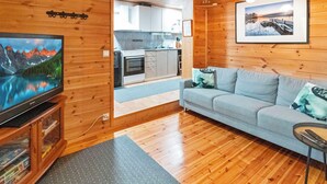 A cozy cabin interior with a wooden interior, a sofa, a television, and a kitchen area visible through an open door.
