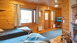 A cabin with two beds, a fireplace, a television, and a window with curtains.