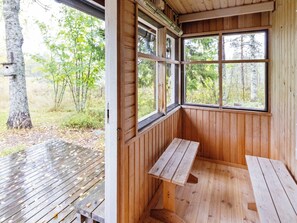 A wooden cabin with a bench and a table outside, a window with a view of trees, and a door.
