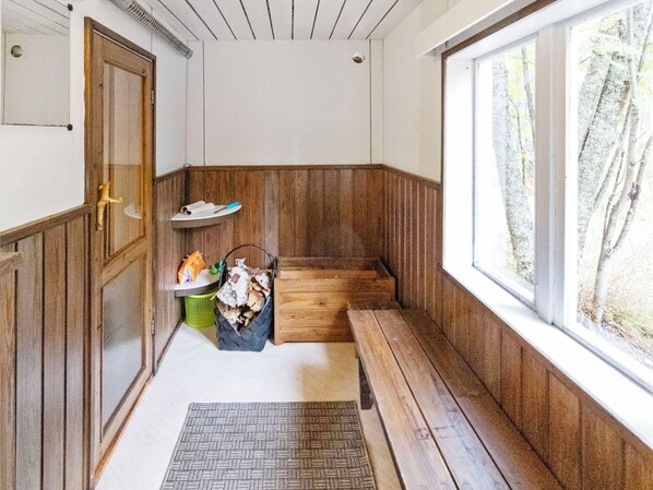 A small, enclosed room with wooden walls and a bench. There is a window with a view of trees and a door with a small animal figure on it.