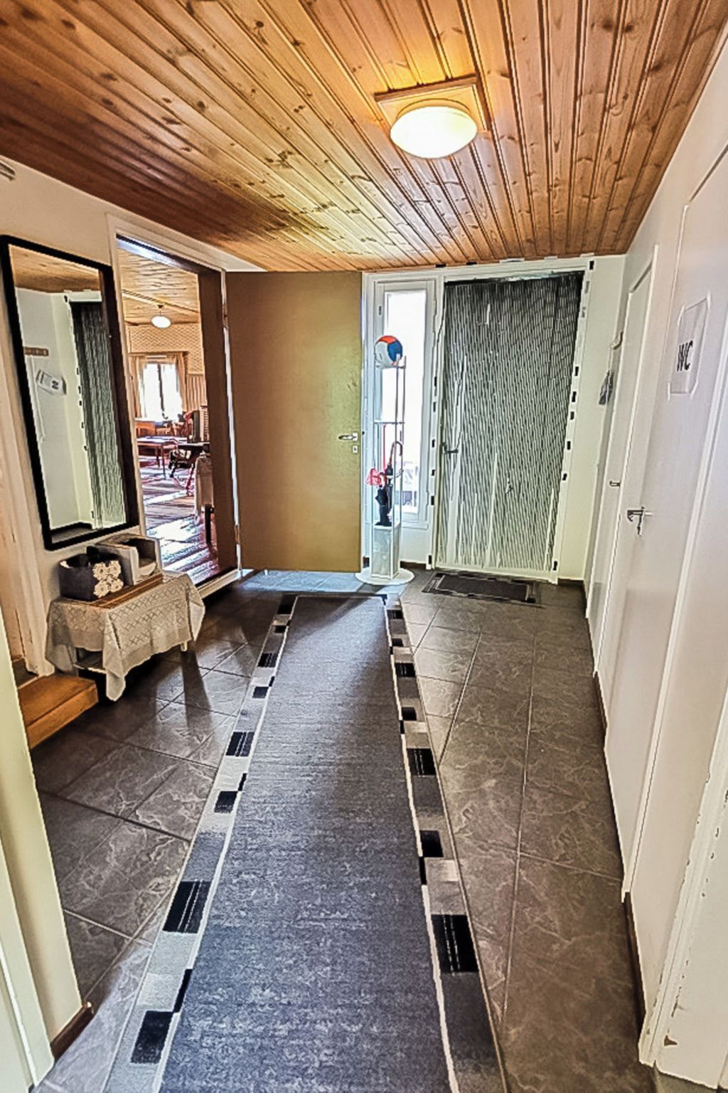 A hallway with a wooden ceiling, a tiled floor, and a door leading to a room.