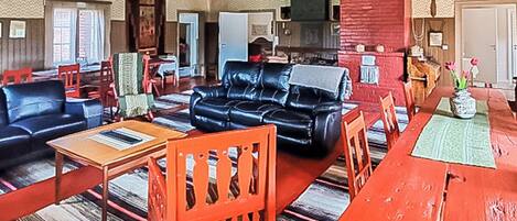 Ein geräumiges Wohnzimmer mit einer schwarzen Ledersofa, roten Sessel, einem Holzespeisetisch und einer Küchenzeile im Hintergrund.
