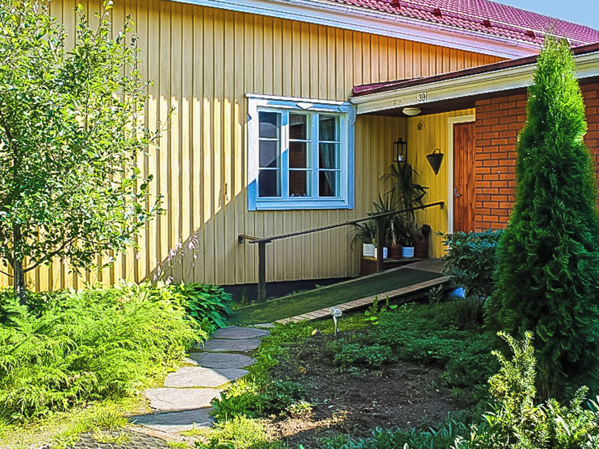 Et gult hus med rødt tag, en fordør, et vindue og en lille veranda.