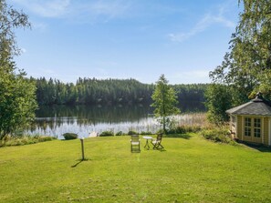 Une propriété au bord du lac, avec une pelouse verdoyante, une petite construction en bois et un bateau amarré près de l’eau.