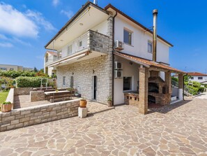 A two-story house with a stone facade, a balcony, and a stone patio with outdoor furniture.