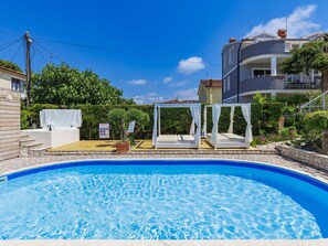 A swimming pool with a clear blue water surface, surrounded by a garden with various plants and a white gazebo structure.