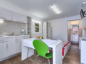 A compact, modern kitchen with white cabinetry, a dining table with a green chair, and a small refrigerator.