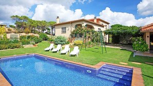 A swimming pool with lounge chairs, a house with a red roof, and a garden with various plants. - Vacation home Marina by Interhome (Vidreres)