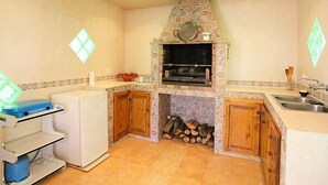 A compact kitchen with a stone oven, wooden cabinets, and a countertop with a sink. - Vacation home Marina by Interhome (Vidreres)