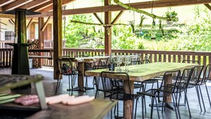 An outdoor patio with wooden tables and chairs, a hanging plant, and a view of greenery. - Lembondel by Interhome (Tiarno di Sotto)