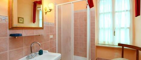 Un baño con lavamanos, cabina de ducha, una silla y ventana con cortinas.
