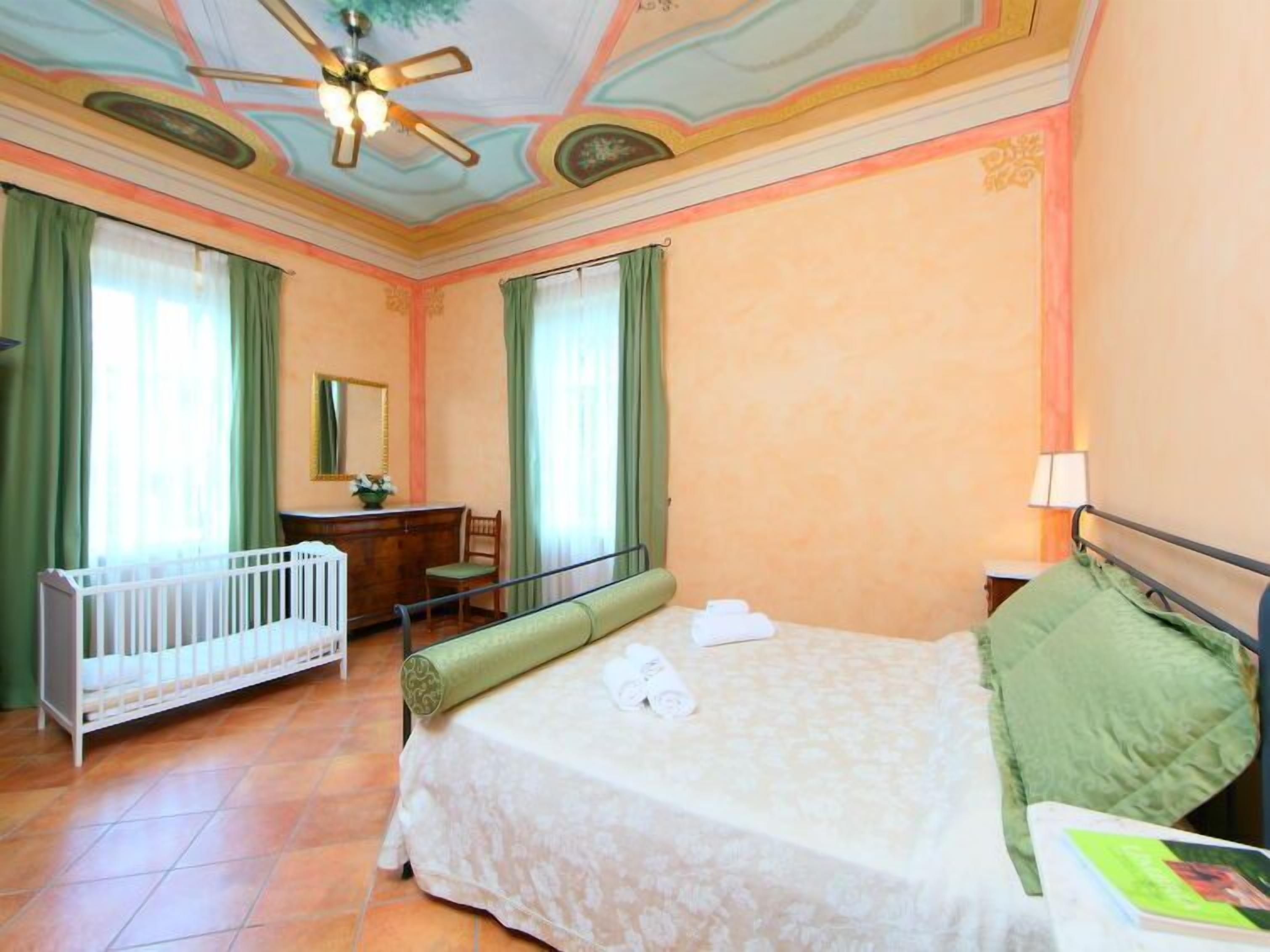 Une pièce comprenant un lit, un bureau, une chaise, un berceau et un ventilateur de plafond.