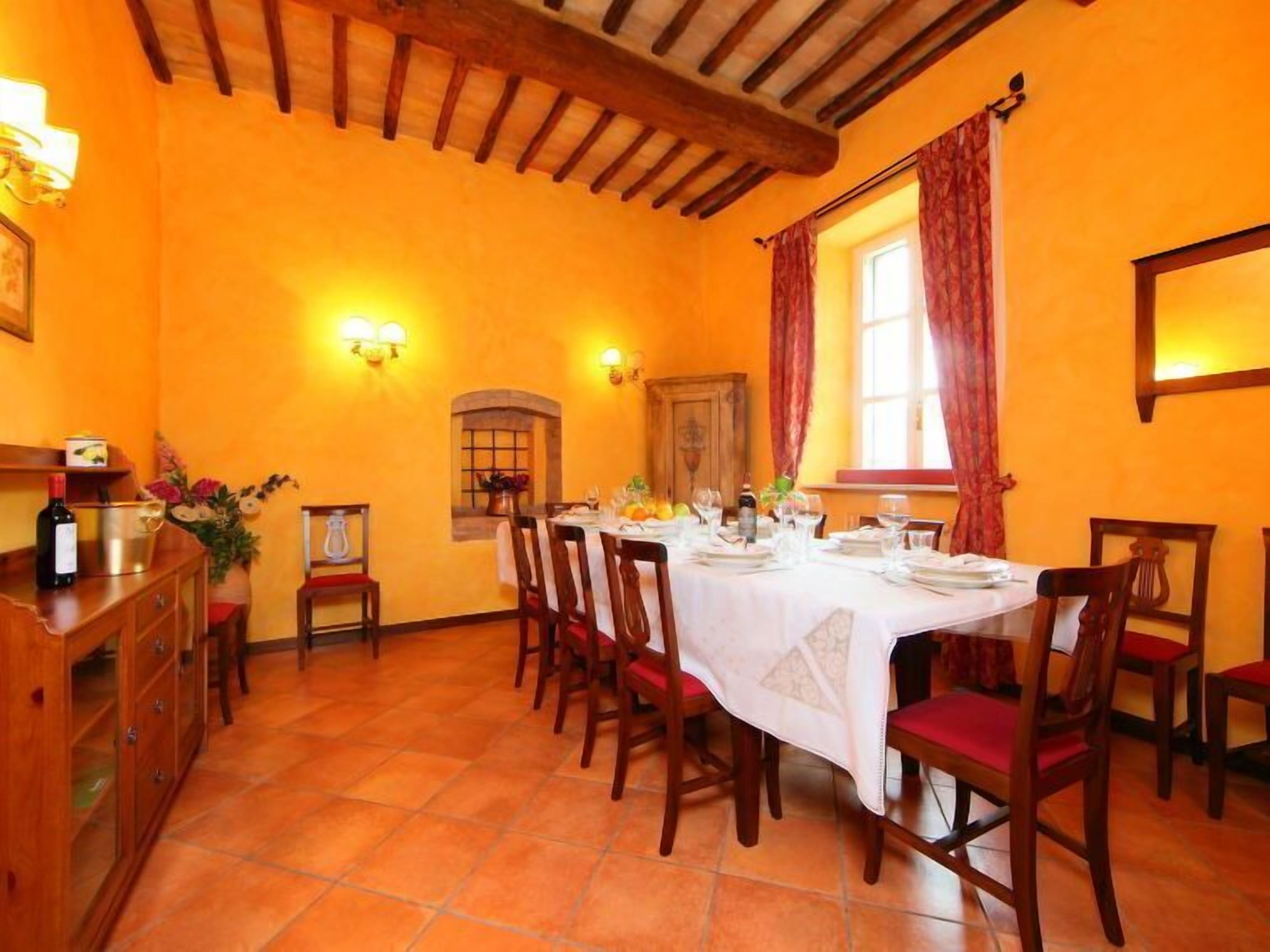 Una sala da pranzo con un tavolo di legno apparecchiato per sei persone, circondato da sedie con cuscini rossi.
